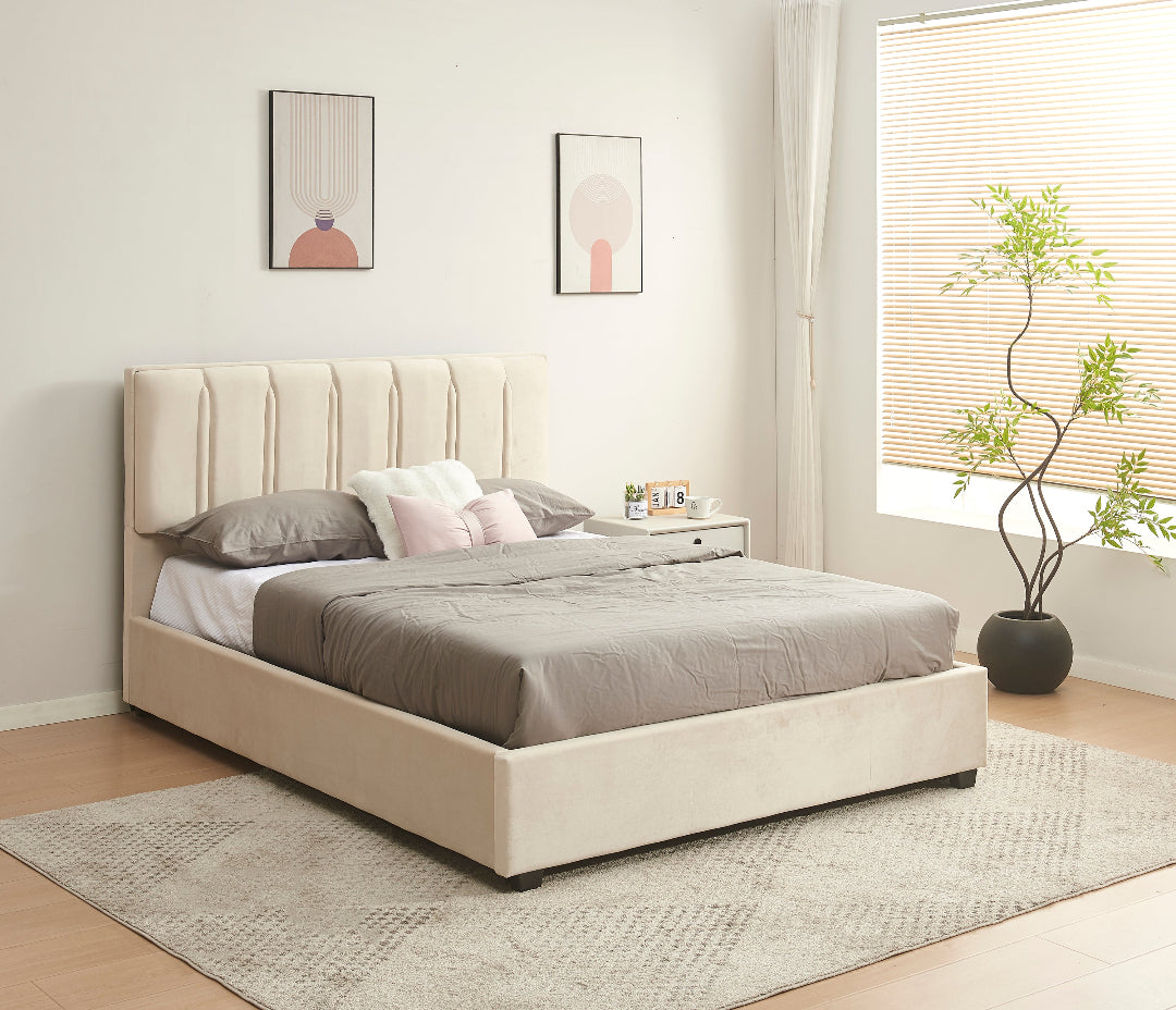 Beige upholstered bed with gray bedding in a room with a window and plant.
