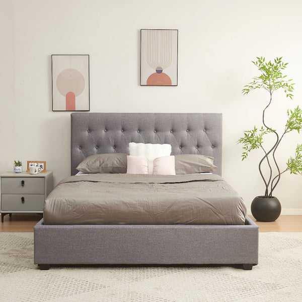 Gray upholstered bed in a room with a nightstand, plant, and wall art.